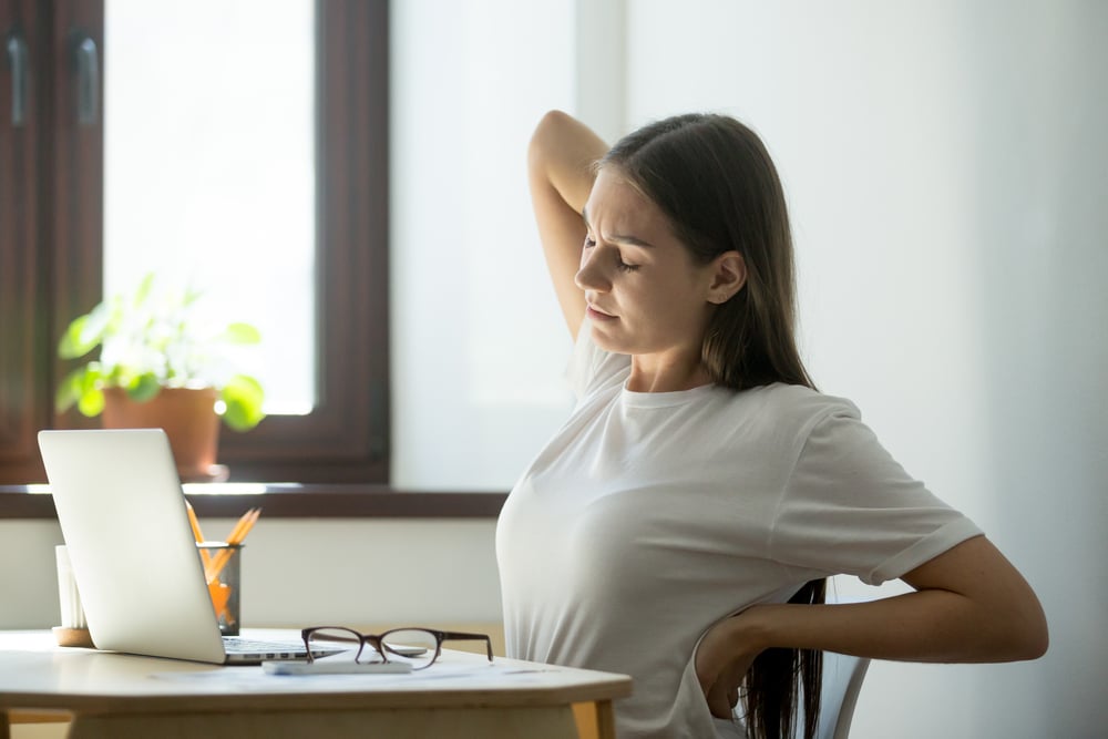 Woman stretching and clutching her back in pain and in need of ketamine infusion treatment.