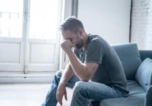 Man with CRPS sitting on a couch with his head in his hand, suffering from depression from his pain