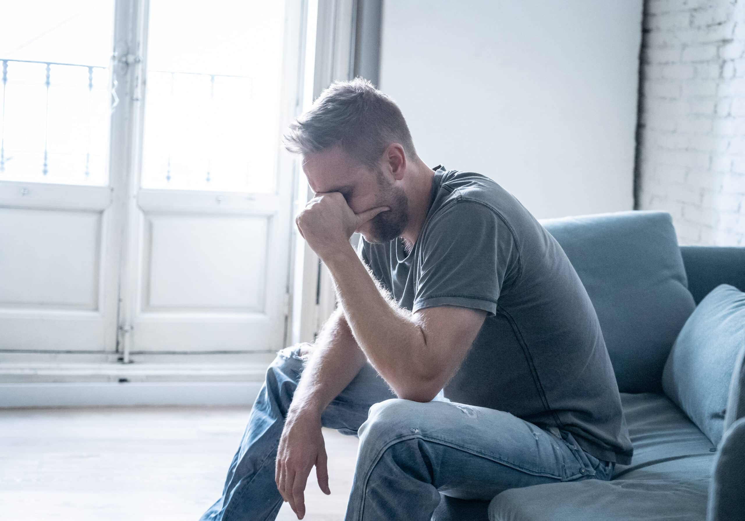 Man with CRPS sitting on a couch with his head in his hand, suffering from depression from his pain