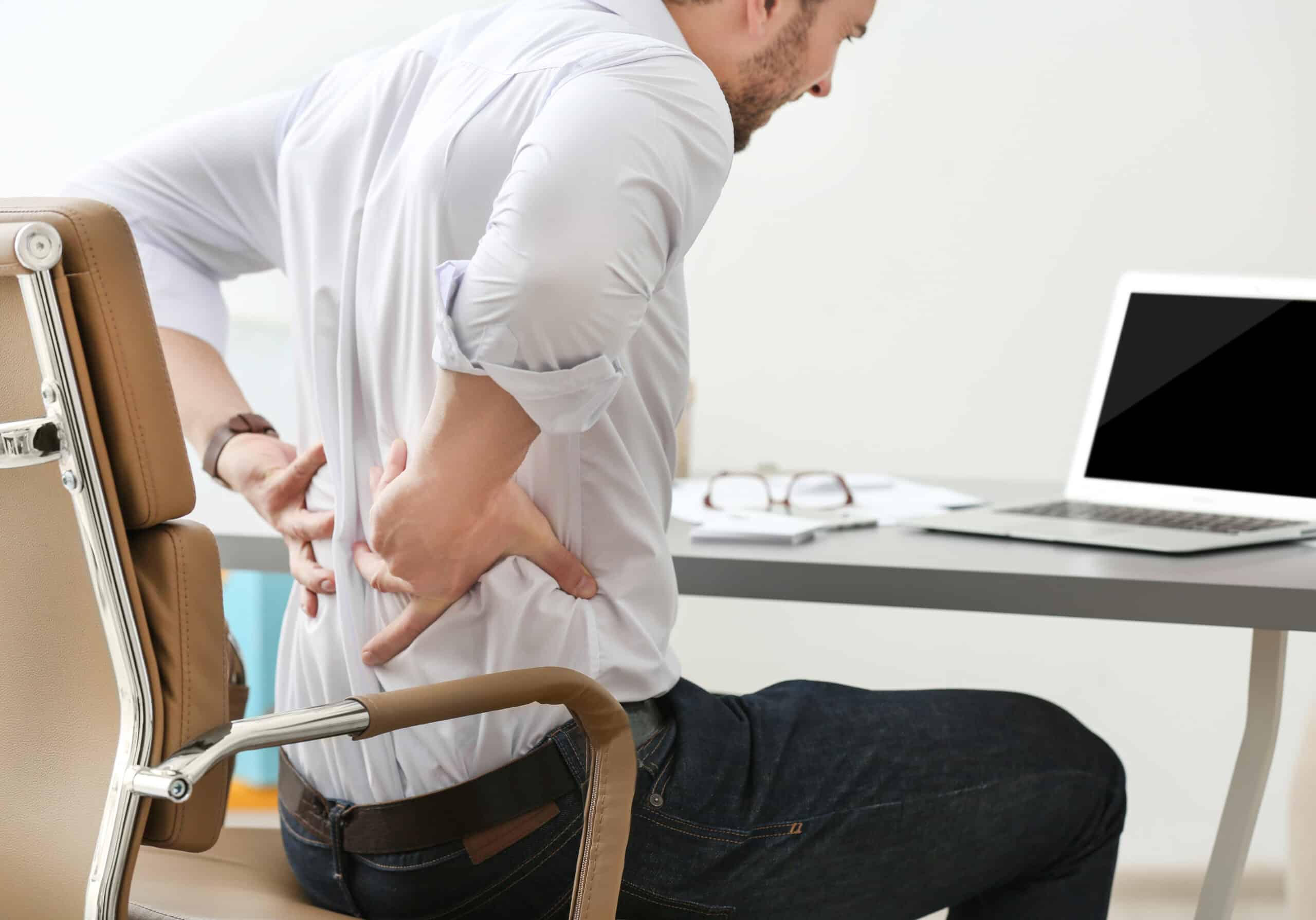 Man sitting at a work desk and clutching his back in pain from lumbar spinal stenosis