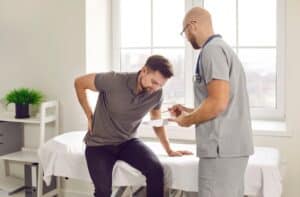 Man holding his lower back in pain during a doctor's exam to determine a targeted pain management plan.