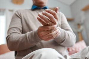 Close-up of an older man rubbing at his hand, suffering from complex regional pain syndrome.