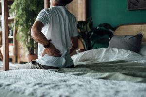 Close-up of a older man sitting on a bed and clutching his lower back in pain, needing lumbar decompression.