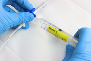 Close-up of a provider administering ketamine into a patient's infusion therapy for pain management.